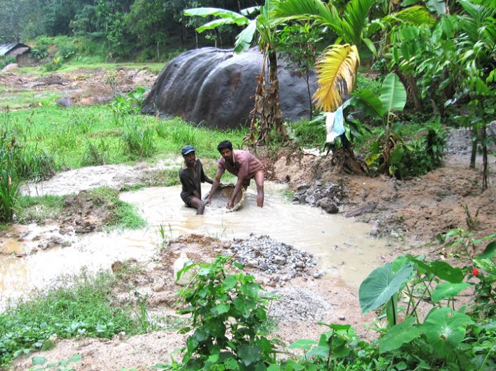 Two gem miners working knee deep in water with a sieve – are paid no wages and get only meals
