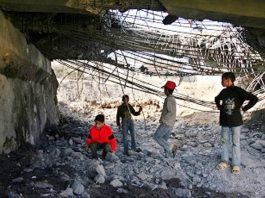 Palestinian children play under a huge hole in a bridge at Beit Hanoun in the Gaza Strip after it was blown up by an Israeli missile