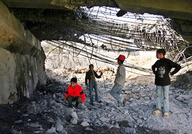 Palestinian children play under a huge hole in a bridge at Beit Hanoun in the Gaza Strip after it was blown up by an Israeli missile