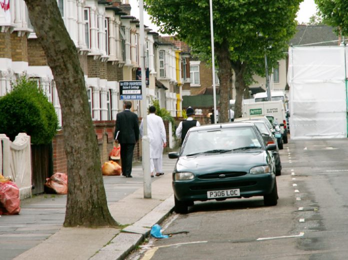 Police escort resident to his door in Lansdown Road, Forest Gate, yesterday midday, with number 46 hidden by plastic sheeting