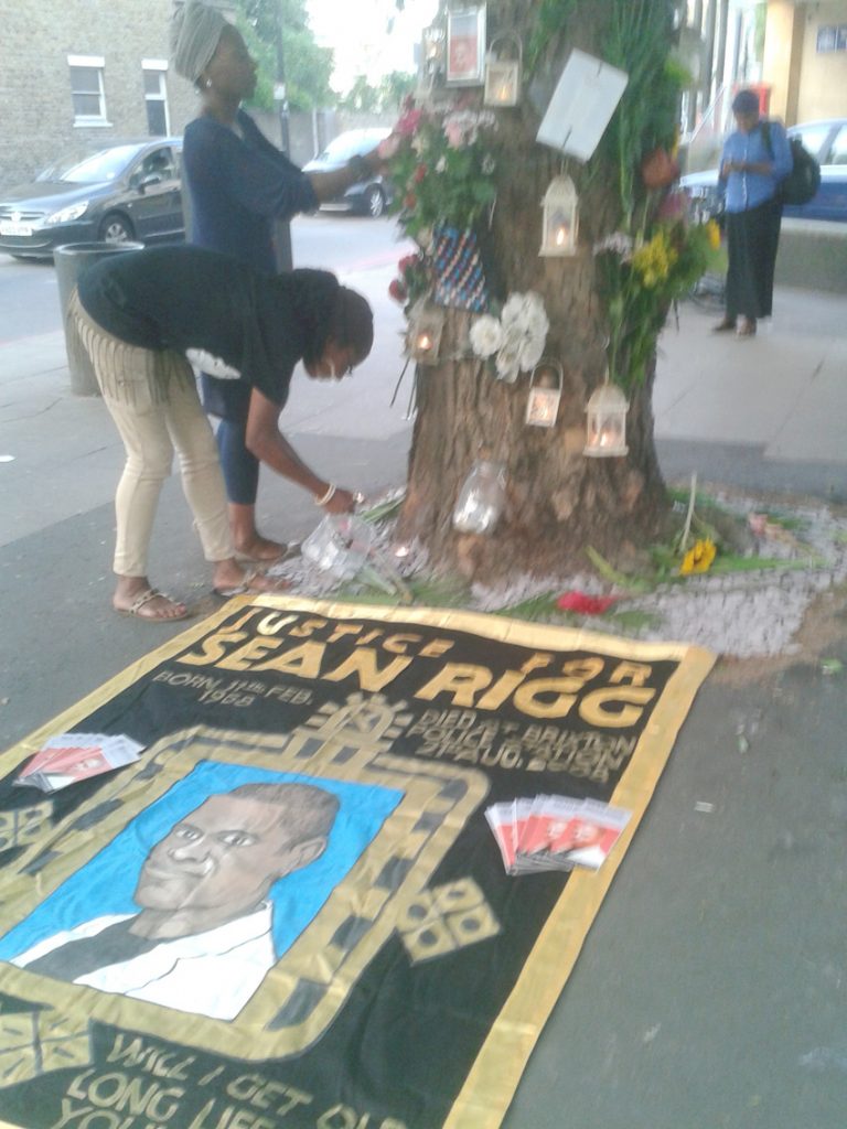 The banner of the Sean Rigg Justice and Change Campaign under a memorial to him outside Brixton Police station