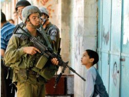 An Israeli soldier casually points his gun at a Palestinian boy