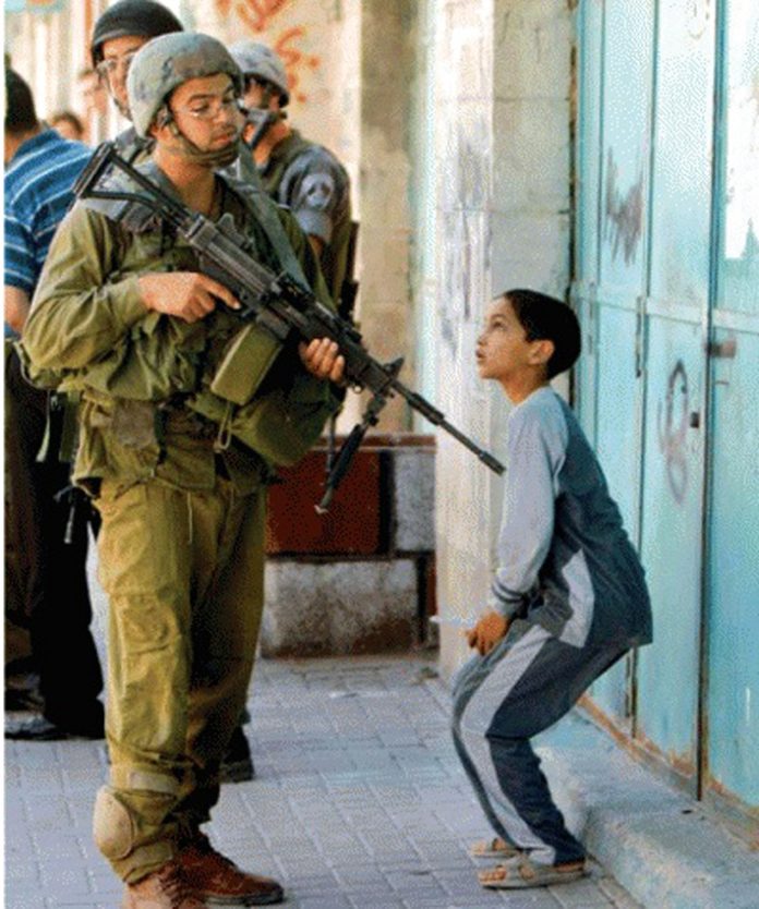 An Israeli soldier casually points his gun at a Palestinian boy