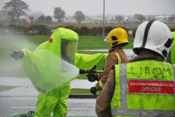 Firefighter in decontamination suit being hosed down