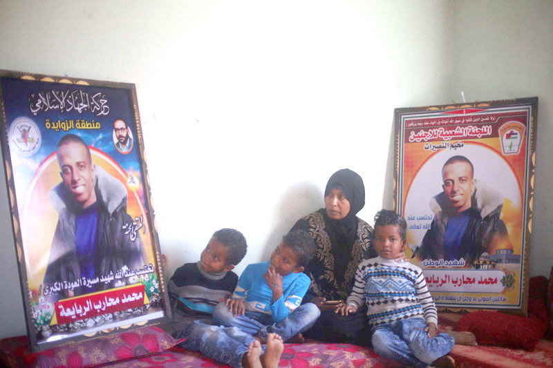 Muhammad al-Rabaia’s mother and three sons sit beside posters honoring their slain father and son. Photo credit: Abed Zagout
