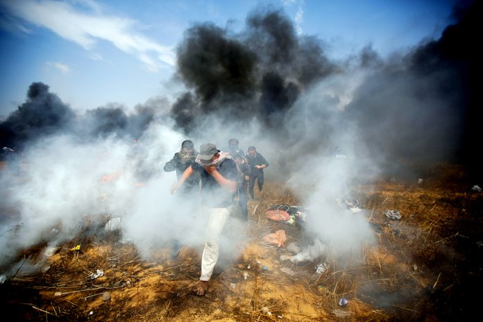 Palestinians emerge through clouds of teargas fired by Israeli troops at the Gaza border on the 6th Friday demonstration yesterday