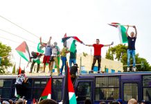 Palestinians in Athens climb on top of police buses and defiantly wave their flags