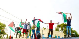 Palestinians in Athens climb on top of police buses and defiantly wave their flags