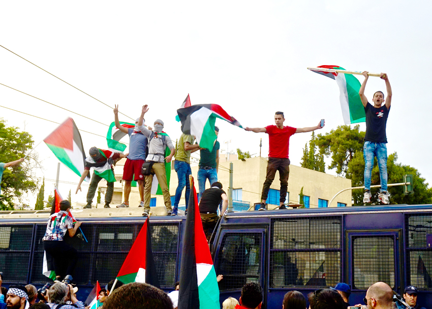 Palestinians in Athens climb on top of police buses and defiantly wave their flags