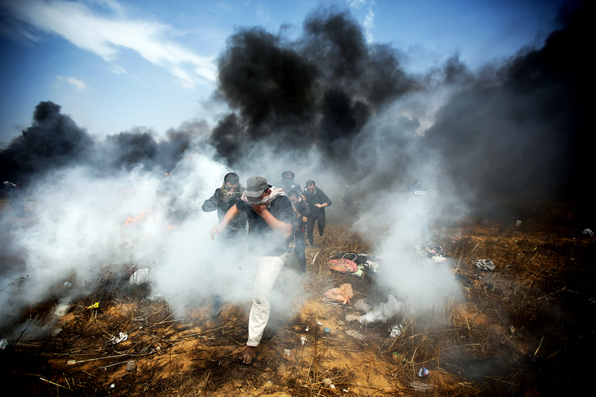 Young Palestinian demonstrators escaping the bombardment of tear gas and bullets from Israeli Defence Forces at the Gaza-Israel border fence