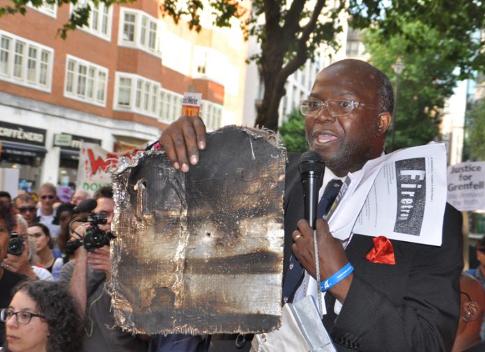 A local resident holds up charred remains of Grenfell Tower cladding – 468 buildings across the UK are clad in the same flammable aluminium composite – the Tories refuse to ban it