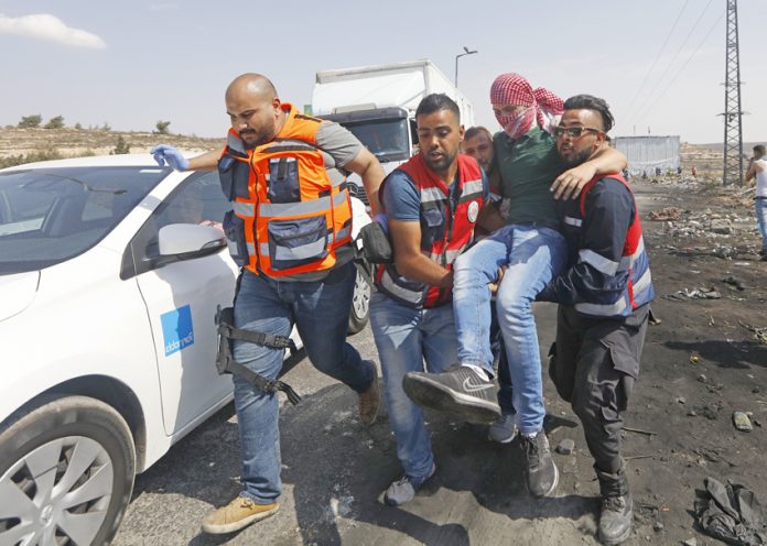 Medics help a Palestinian student on a protest against Israel’s racist Nation State law after he was shot by Israeli troops