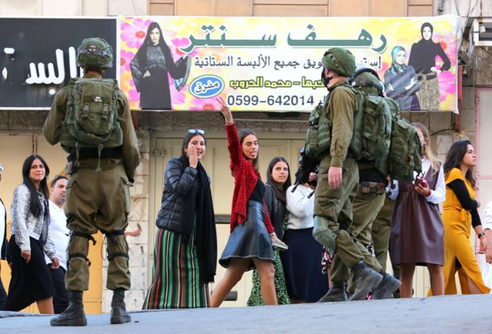 Palestinian girls in Hebron defy the occupying Israeli troops (above) after they had blocked off a road in the city on Friday (below) to allow access to Israeli settlers